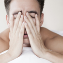Man in bed with hands covering face